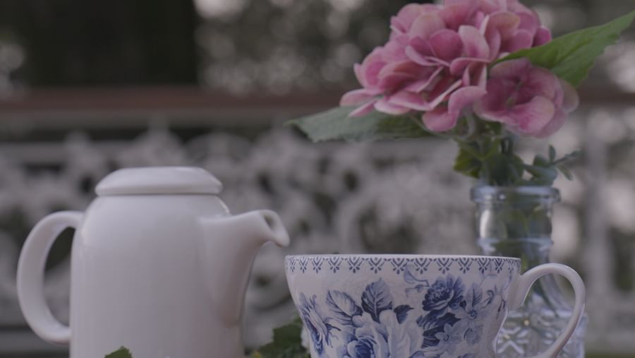 Outdoor tea setup with floral crockery and fresh pink flowers in soft focus - Mayfair Cafe & Suites, Dalhousie