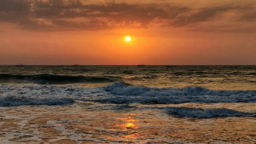 A sunset at a beach with waves crashing the shore under a vibrant sky