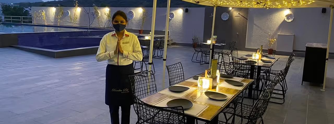 Waiter serving at a set table, string lights, evening setting.