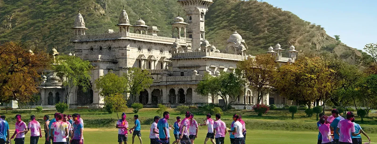 facade image of the mayo college with a huge green lawn in the foreground with adolescent kids roaming around