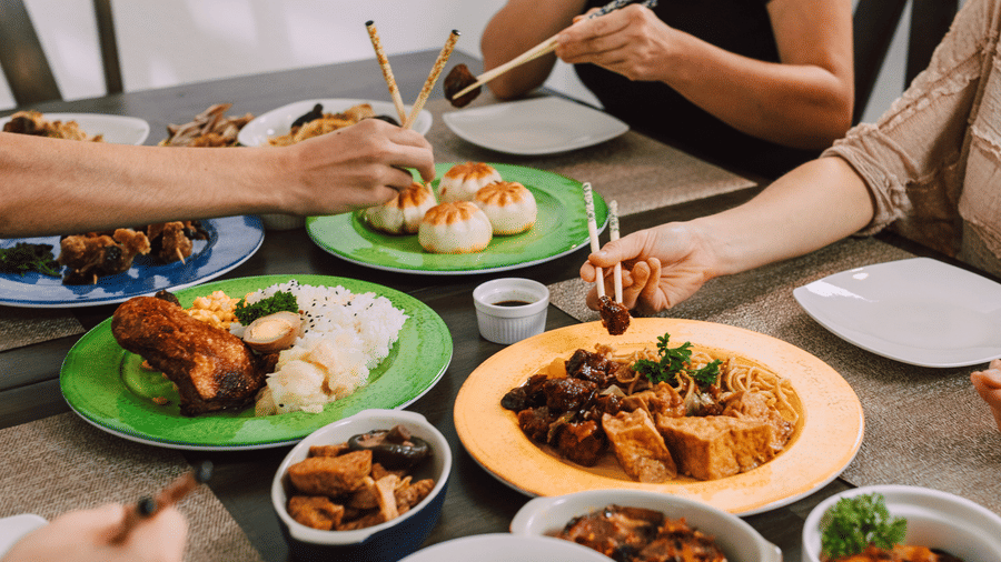 People sharing a meal at a table using chopsticks and cutlery.