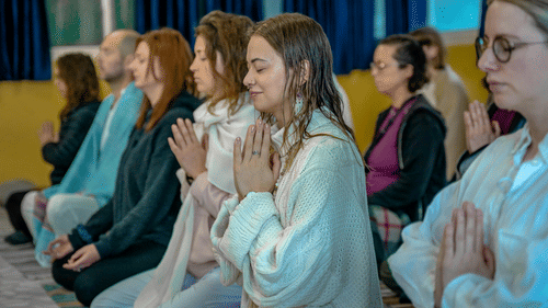 a group of devotees with their palms joined seated in a room
