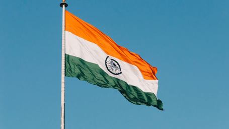 Indian flag flying on a flagpole against a clear blue sky.
