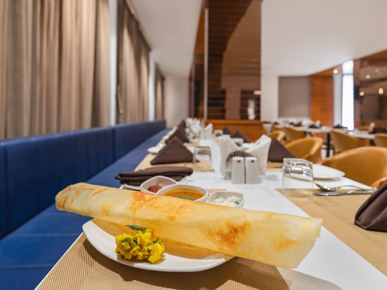 A long, thin crepe with a side of filling sits on a plate on a set table in a restaurant - Lords Eco Inn Ambaji.