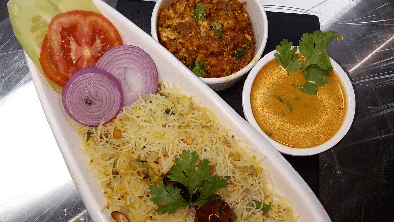  A white oval plate filled with yellow rice, garnished with cilantro. Accompanied by a small bowl of chutney and a half lemon.