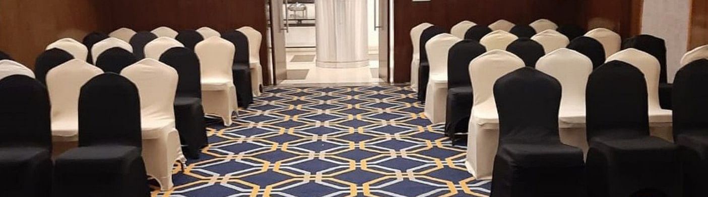 A well-arranged conference hall at the banquet hal, The Cunningham Hotel, featuring elegant black and white chairs, a vibrant geometric-patterned carpet, warm lighting, and a sophisticated ambience