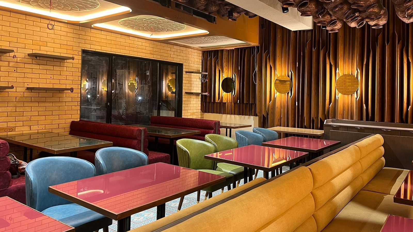 A dining area showing blue and red seating, a brick wall, unique wooden chandeliers, and decorative wall plates.