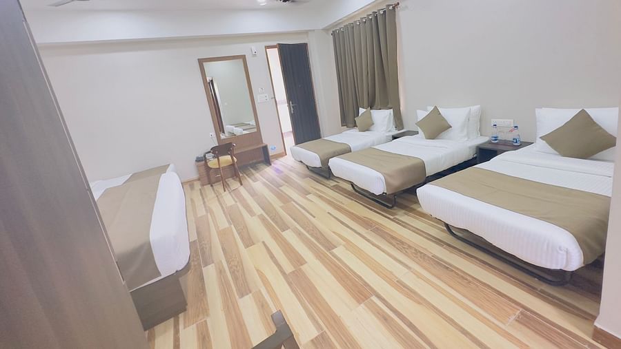 A spacious hotel room features double beds with white and gold bedding and a ceiling fan - Kankidham Lords Inn