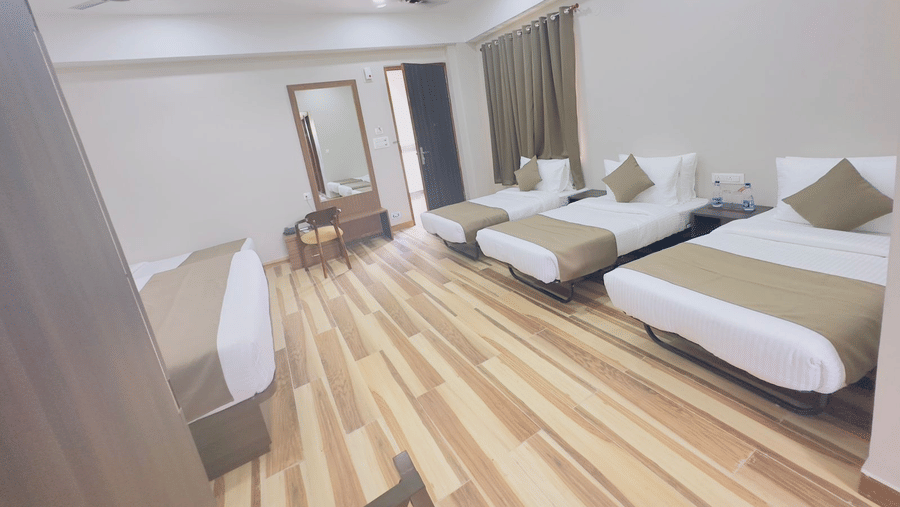 A spacious hotel room features double beds with white and gold bedding and a ceiling fan - Kankidham Lords Inn