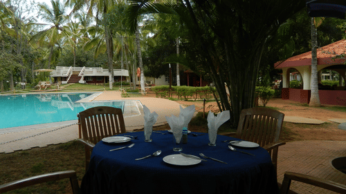 Image of Poolside Garden at Fantasy Golf Resort Bangalore featuring a dining setting by the pool in the shade during daytime