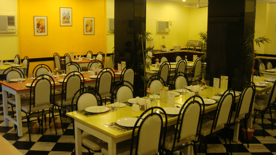 Main dining area of the hotel restaurant showing arranged tables and chairs against a bright yellow accent wall - Hotel Pandian