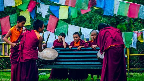 a group of monks playing drums in a park and having fun around a bench