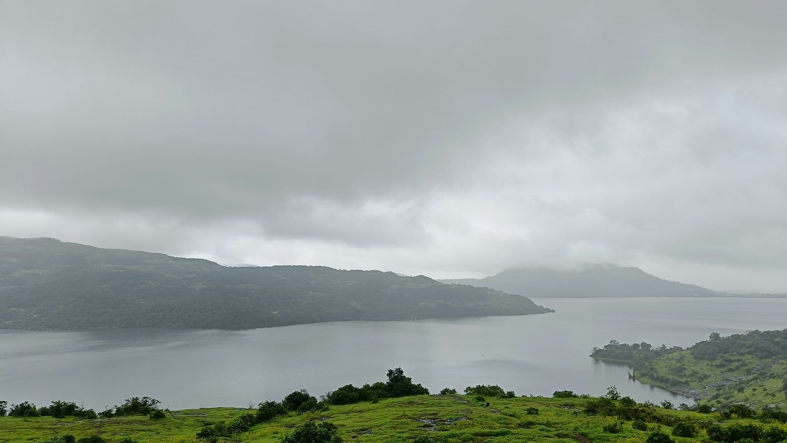 Overcast skies above a tranquil lake surrounded by green hills and foliage
