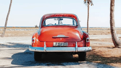 A vintage car parked near a beach with coconut trees next to it.