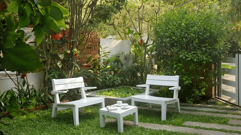 White garden seating set on a green lawn surrounded by trees and plants at Amanvana Spa Resort in Coorg.