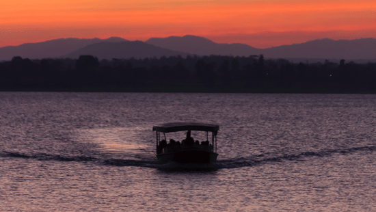 A boat cruising through a river during sunset with the hills visible in the background.