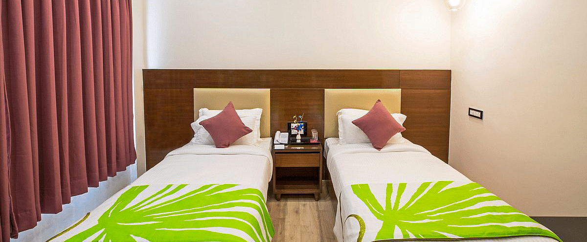 Front view shot of two single beds in Deluxe Twin Room separated by a bed side table in the middle at Regenta Inn DLS.