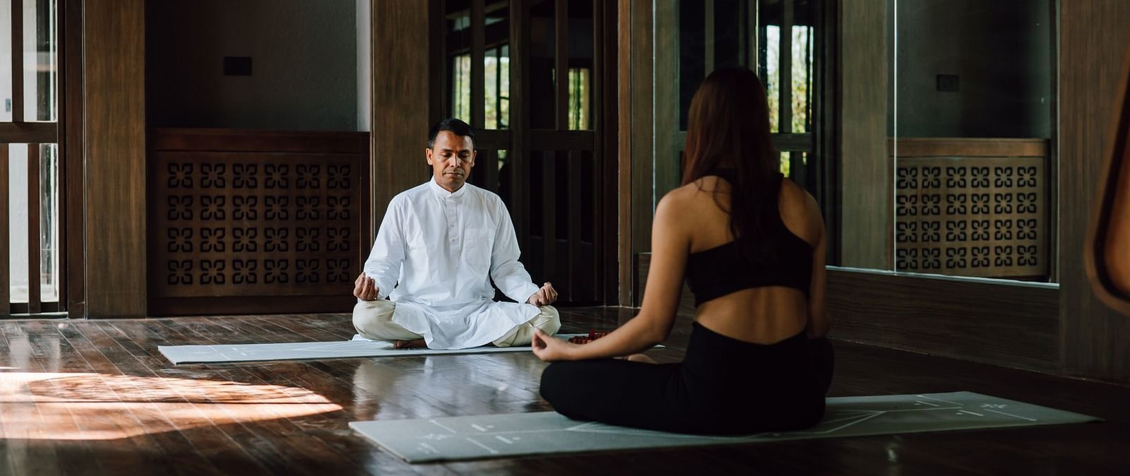 A man in white attire teaching a woman meditation indoors.