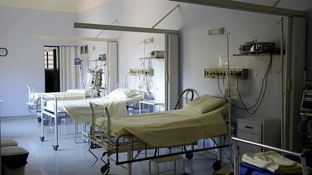 A hospital room with empty beds, medical equipment, and white curtains.