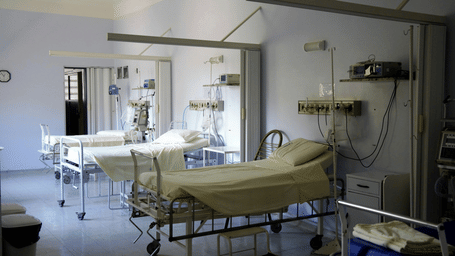 A hospital room with empty beds, medical equipment, and white curtains.