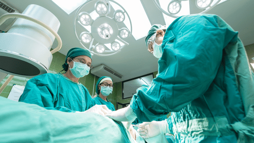 Several surgeons operating on a patient wearing green surgical gowns and masks in an operating theatre.