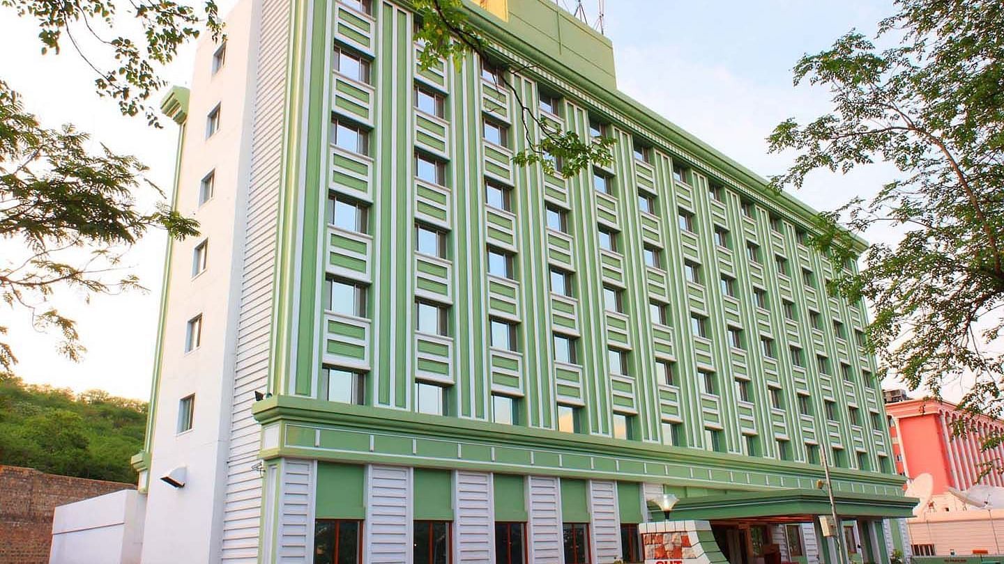 A multi-story green hotel building flanked by trees at Tara, Comfort Hotel in Hyderabad - Ramoji Film City.