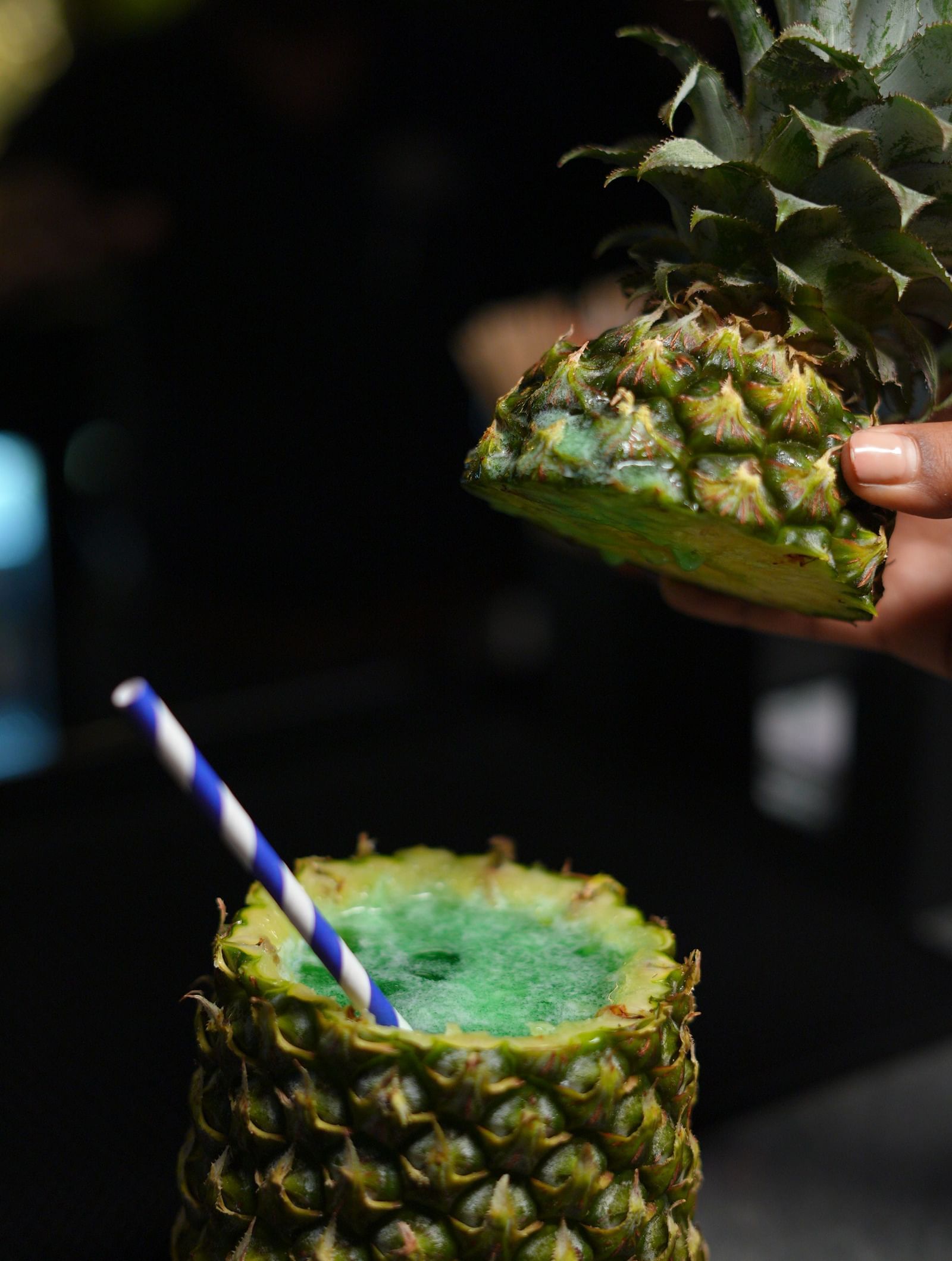 A hand preparing a pineapple drink with a straw, close-up shot at Cenneys Gateway.