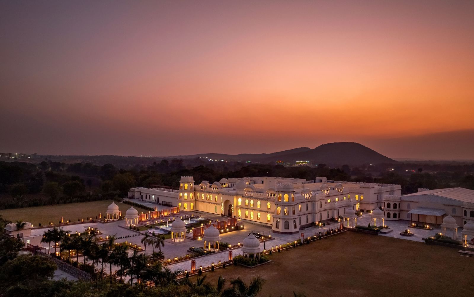 Aerial view of Kesar Bagh Palace illuminated with lights with mountains in the background.