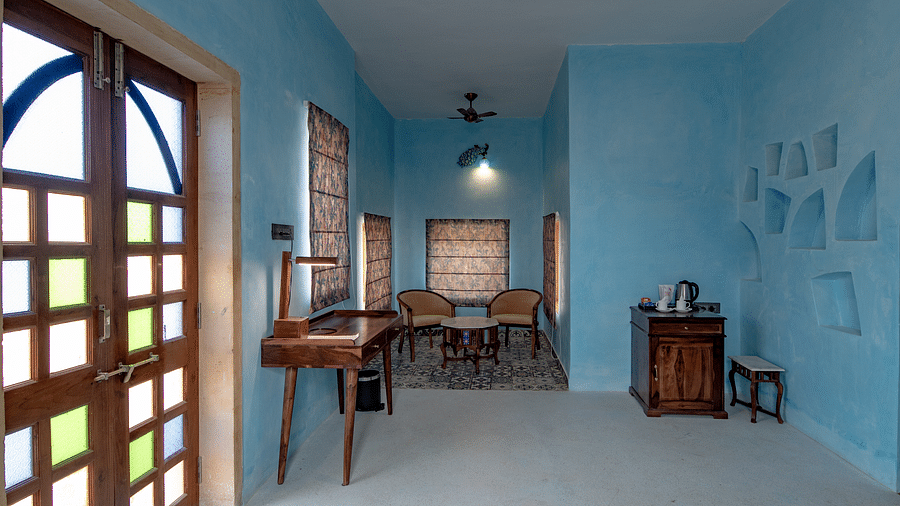 An image of an indoor seating area with chairs and tables along with a work desk and table at a corner where  tea and coffee maker is kept - Karwaan Jaisalmer