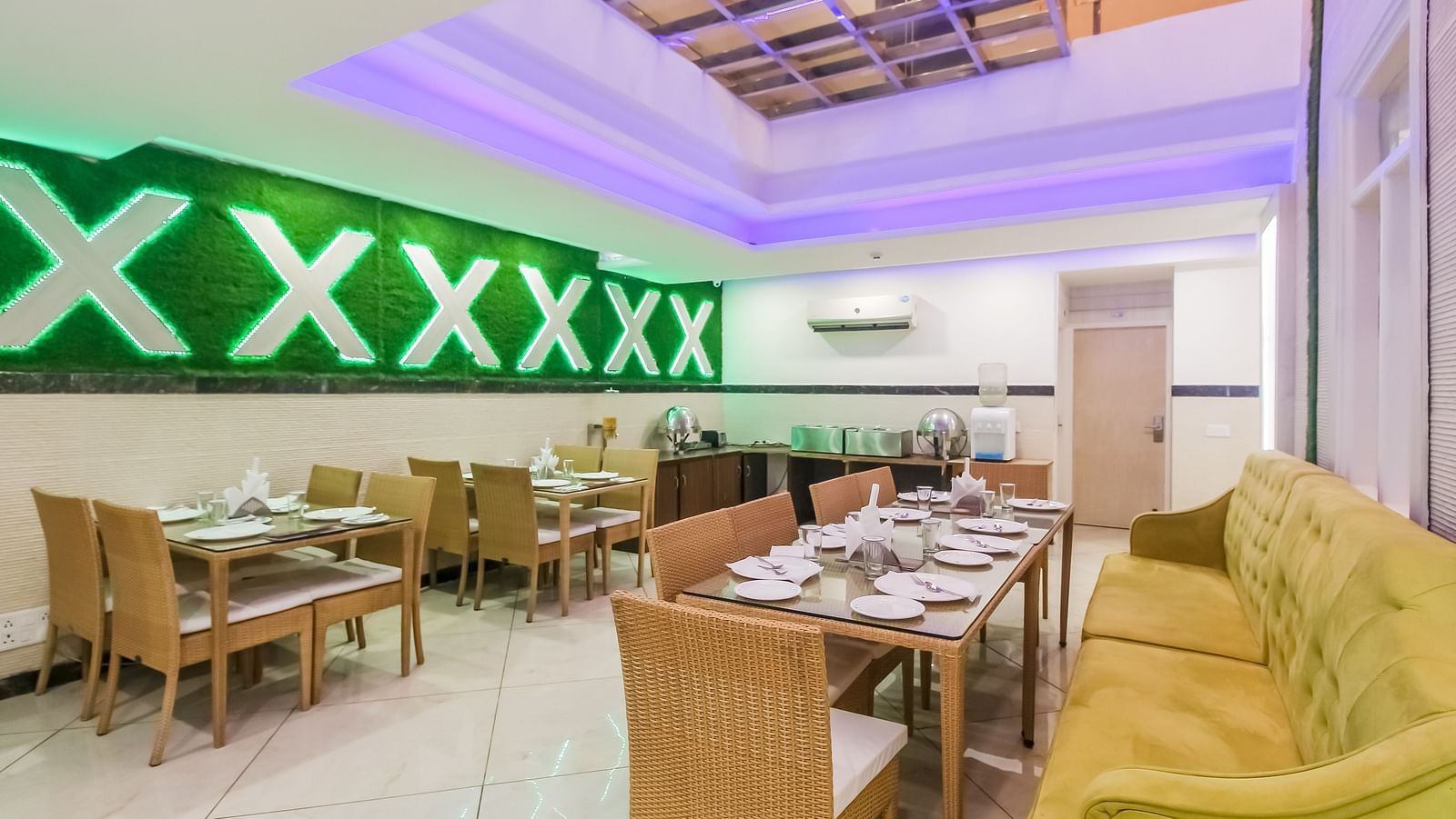 A restaurant interior with a long tufted sofa, wooden tables and chairs, a decorative wall design, and a tiled floor, lit by soft lighting. - Hotel Diamond Plaza, Chandigarh.