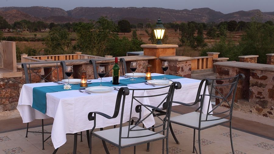 Rooftop dining setup with a white tablecloth, candles, and wine bottle, overlooking scenic hills at sunset at Juna Mahal
