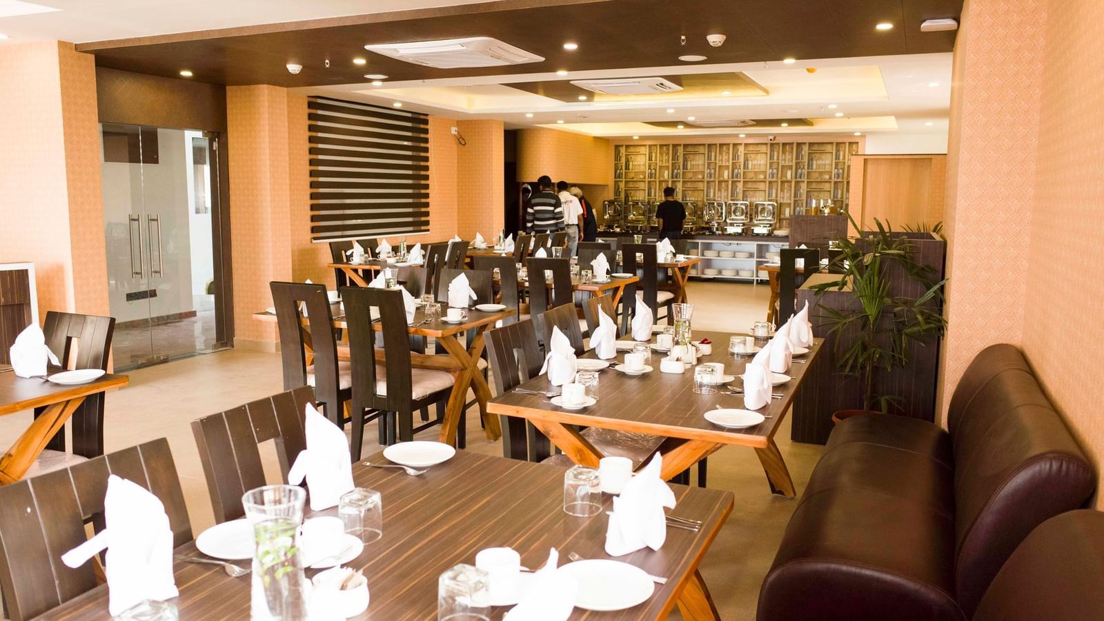 A hotel restaurant with set tables, dark chairs | Daksh The Madhuvan Suites