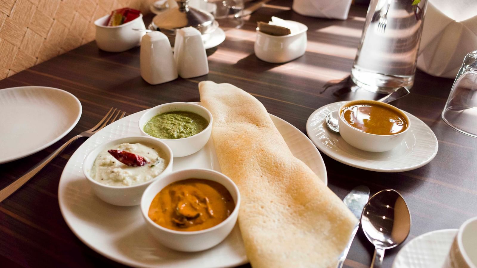 A South Indian meal with dosa and various chutneys served on a plate | Daksh The Madhuvan Suites
