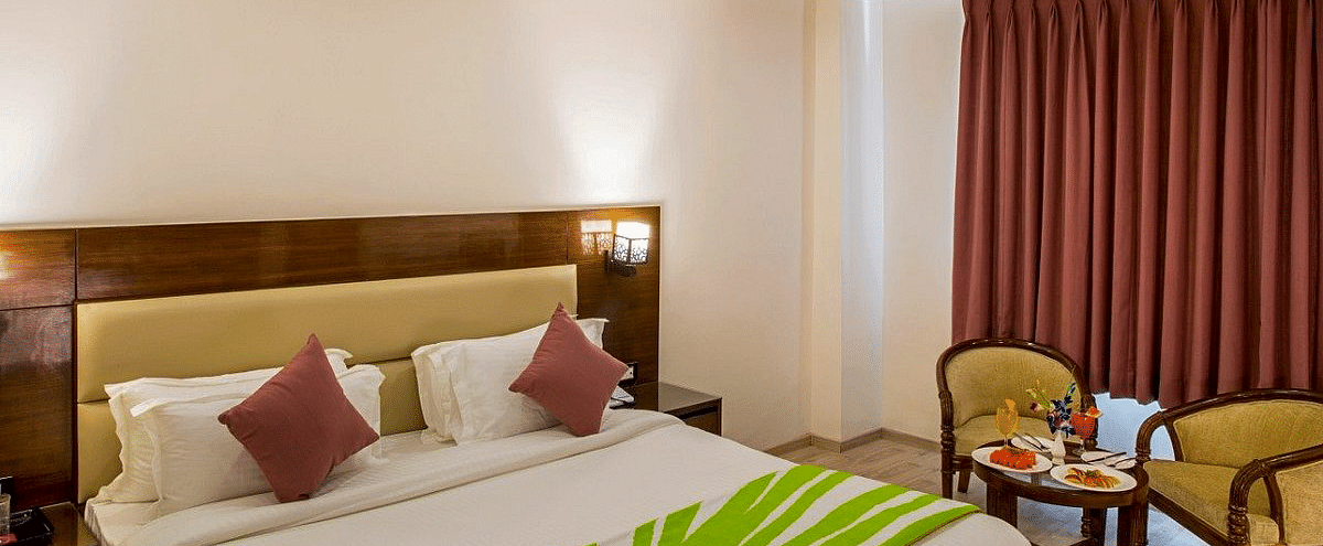 The Premium Room featuring a double bed with a green coloured bed runner over it along with a common seating area in the corner at Regenta Inn DLS.
