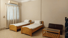 Interiors of a room at Lake Side Resort Neermahal featuring 2 wooden beds, an A/C unit, a small wooden table and tiled floors.