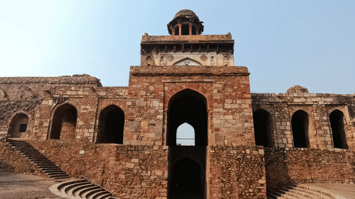 Facade view of the entrance to Chandragiri fort with arches on the side of the building and blue sky in the background.