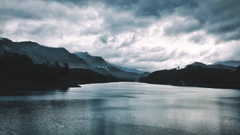 A landscape with a dark, cloudy sky reflected in a calm lake.