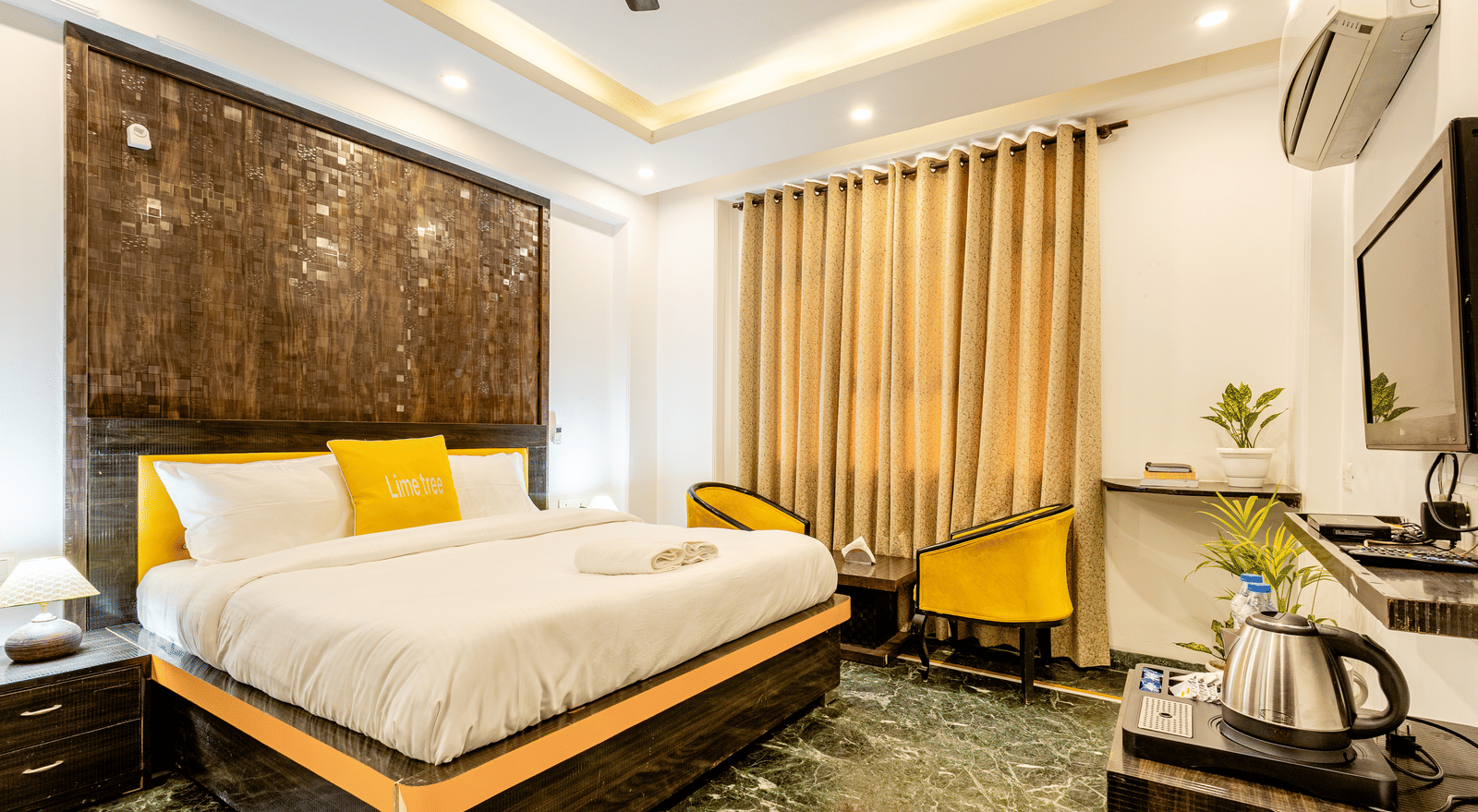 Side and wide angle view of the king size bed, two chairs and a television in the superior king room at Lime Tree Hotels and Banquet Hall Near Huda Metro, Gurgaon