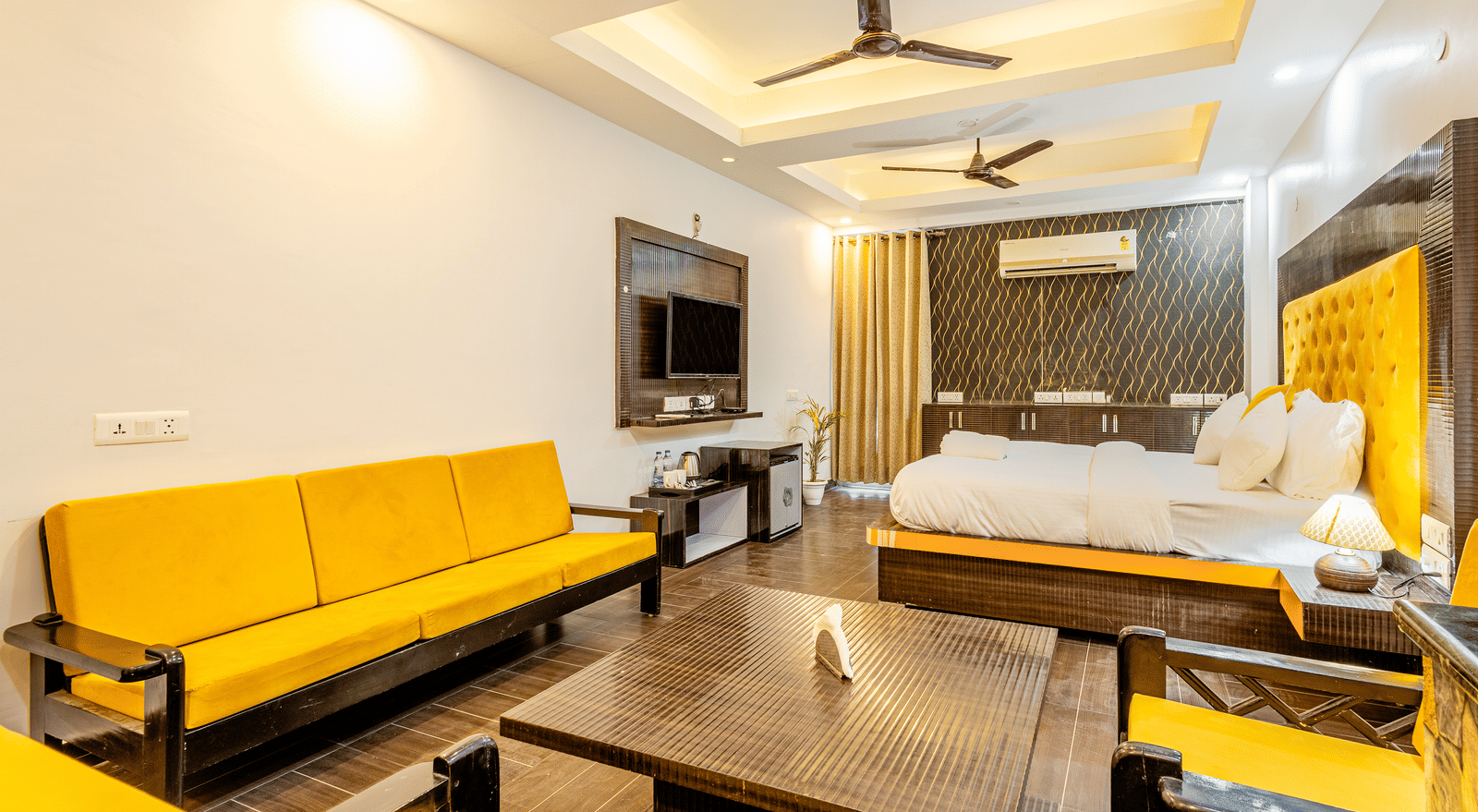 Yellow sofa in the living area and the king size bed with television in front of it at Lime Tree Hotels and Banquet Hall Near Huda Metro, Gurgaon