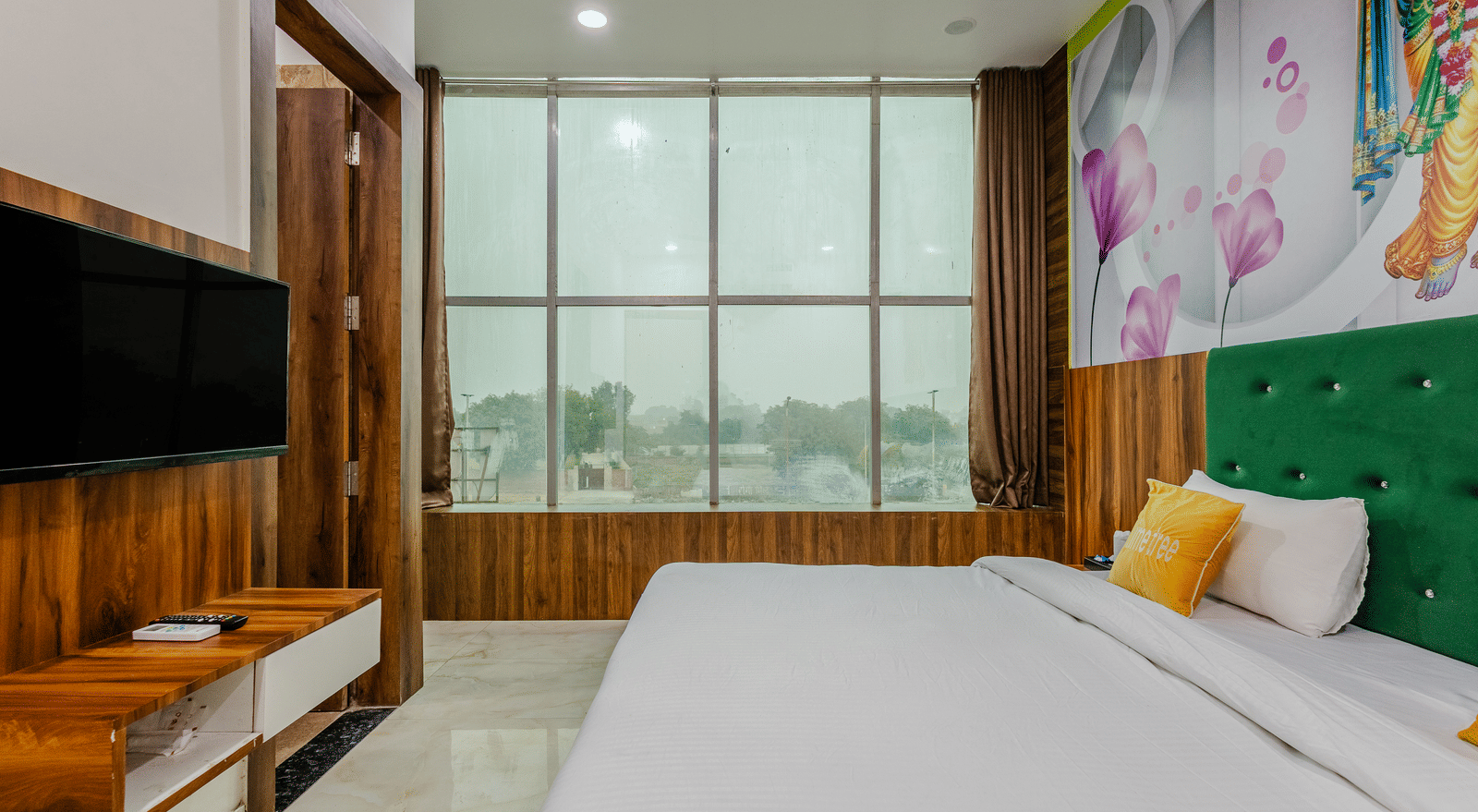 A bedroom with green headboard, floral artwork, and a wall-mounted TV opposite the bed - Lime Tree Hotels & Banquet, Vrindavan