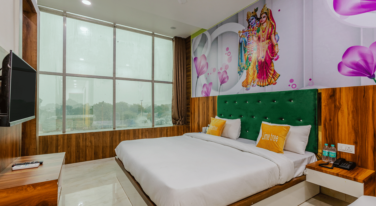 A bedroom with a green headboard, artwork above the bed, large windows, and a wall-mounted television - Lime Tree Hotels & Banquet, Vrindavan