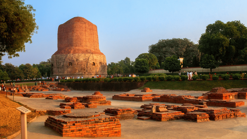 The massive ancient Dhamek Stupa rises above historical brick ruins and manicured lawns at the sacred archaeological site of Sarnath.