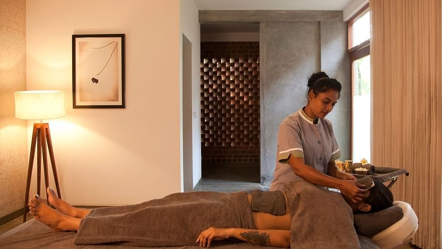 Person receiving head massage on massage table in room with lamp, picture frame, and window - Shreyas Retreat