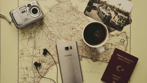 An image of a camera, phone, passport, and a coffee mug placed on top of a map