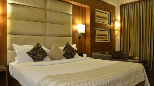 Well lit beddrom at The Bristol Hotel with a king bed, wall mounted lamps and curtained windows.