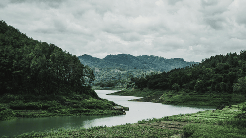 Wide, landscape view of a winding river surrounded by steep, forested hills under an overcast sky.