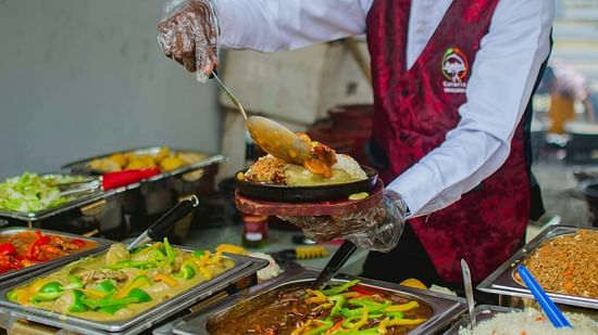 A buffet server in a red vest ladling food onto a hot plate in a buffet setup