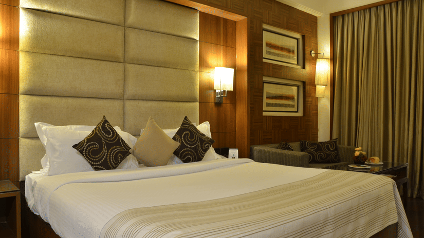 Well lit beddrom at The Bristol Hotel with a king bed, wall mounted lamps and curtained windows.