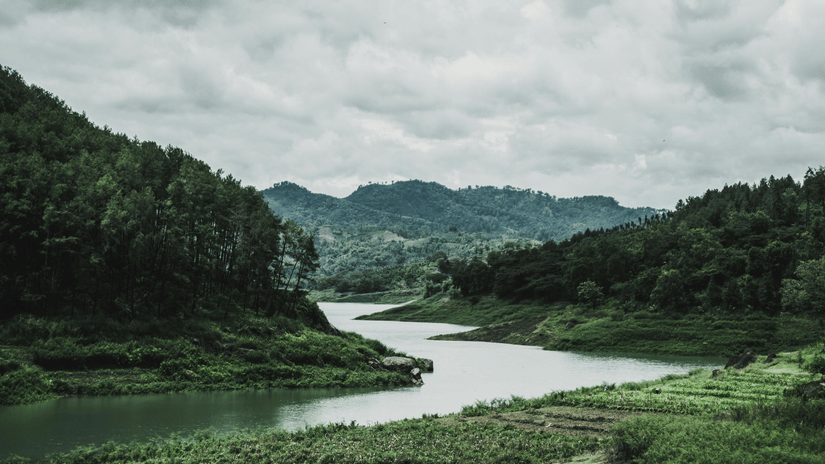 Wide, landscape view of a winding river surrounded by steep, forested hills under an overcast sky.