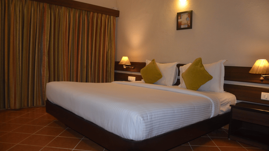 Standard Room in Kodaikanal at Green Pastures featuring a double size bed, a few lamps turned on, bedside table, and a window with curtains drawn.